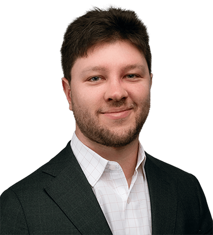 Adam Murrell, a man with short brown hair and a beard, wearing a dark suit jacket and a white checkered shirt, smiles at the camera against a plain background.