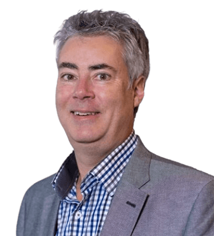 A middle-aged man with gray hair wearing a gray blazer and blue checkered shirt, smiling at the camera against a plain background.