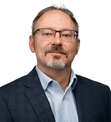 A middle-aged man with glasses, a light beard, and mustache—Alex Campeis—wears a blue suit jacket and light blue shirt, facing the camera with a neutral expression.