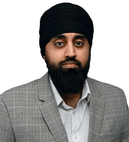 A man with a black turban and beard, resembling Balkarn Khabra, is wearing a gray checkered suit jacket over a white shirt, posing against a plain background.