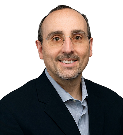 Carlo Pannella, a middle-aged man with short dark hair, glasses, and a trimmed beard, wears a navy blazer over a light-colored shirt as he poses against a blurred background.