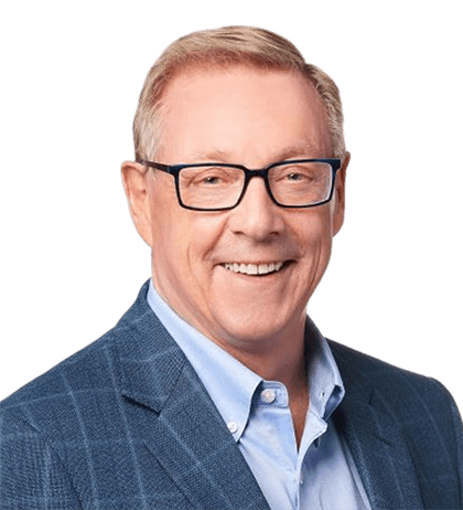 A middle-aged man with short light hair, wearing glasses, a light blue shirt, and a blue checked blazer, smiling at the camera against a plain background.