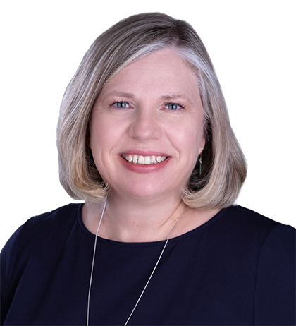 Janine Guenther, a woman with short blonde hair, wearing a navy blue top and a necklace, smiles at the camera against a plain background.