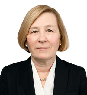 A middle-aged woman, Julianna Varpalotai-Xavier, with short blonde hair wearing a black blazer, white blouse, and a necklace, faces the camera with a neutral expression.