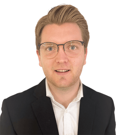 A man with light brown hair and glasses wearing a black suit jacket and white collared shirt, facing forward against a plain background.