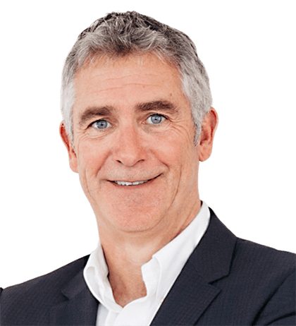 A middle-aged man with gray hair in a dark suit and white shirt, smiling at the camera against a plain background.